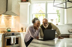 An older couple looks at a laptop computer in their kitchen