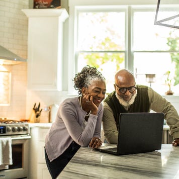An older couple looks at a laptop computer in their kitchen