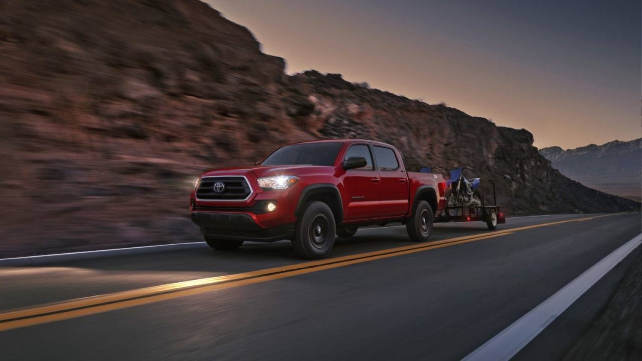 Red Toyota Tacoma pulling a pair of dirtbikes on a trailer at dusk 