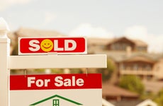 how to sell your house fast - red and white "sold" sign with yellow smiley face in front of suburban house