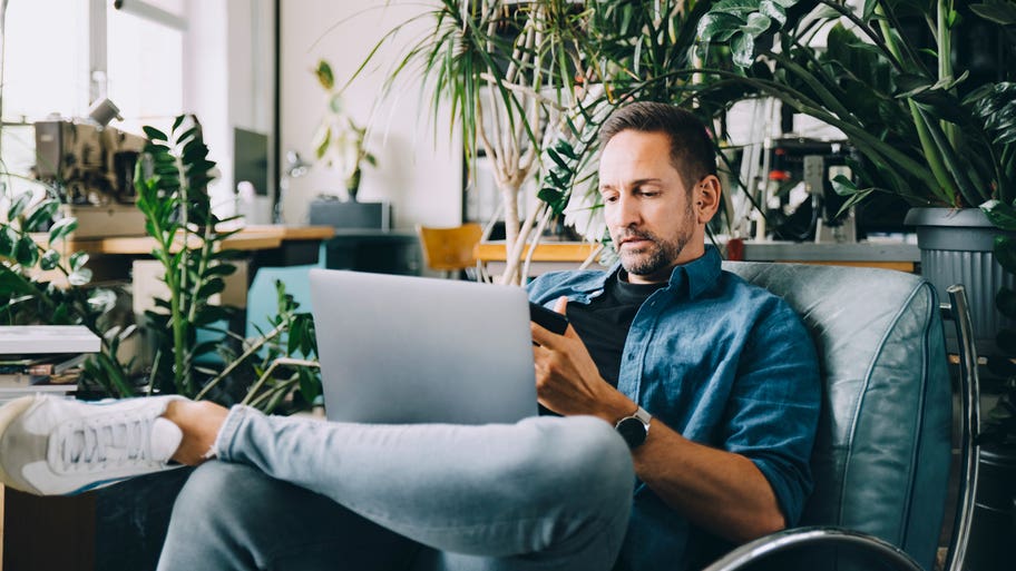 man working on his laptop and looking at his phone