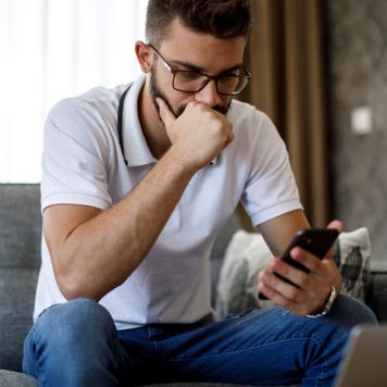 Man with glasses sitting on couch looking pensively at phone