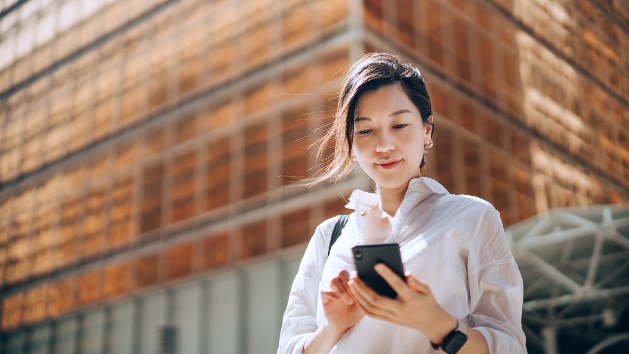 Well-dressed woman in front of big building smiling down at phone