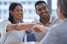 Man and woman smiling together and sitting side by side, woman is shaking hands with financial advisor