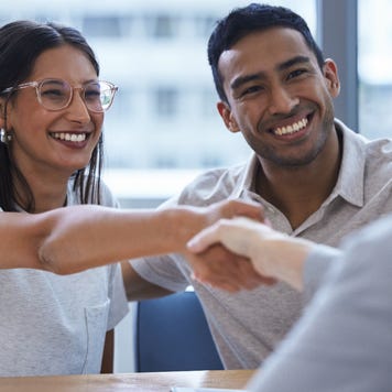 Man and woman smiling together and sitting side by side, woman is shaking hands with financial advisor
