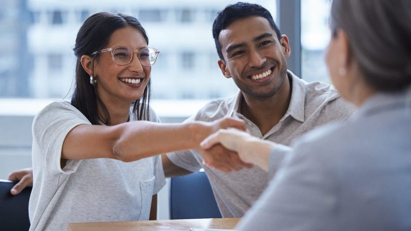 Man and woman smiling together and sitting side by side, woman is shaking hands with financial advisor