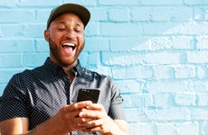 Man in hat smiling at phone with blue brick background