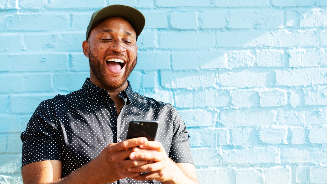Man in hat smiling at phone with blue brick background
