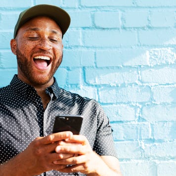 Man in hat smiling at phone with blue brick background