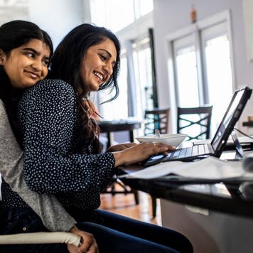 Two Southeast Asian women work on a laptop together.