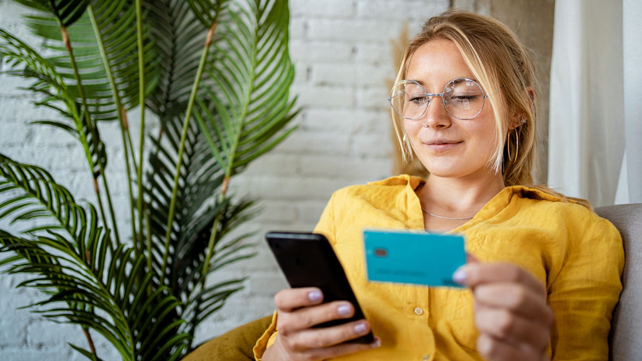 young woman looking at her phone and holding a credit card