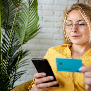 young woman looking at her phone and holding a credit card