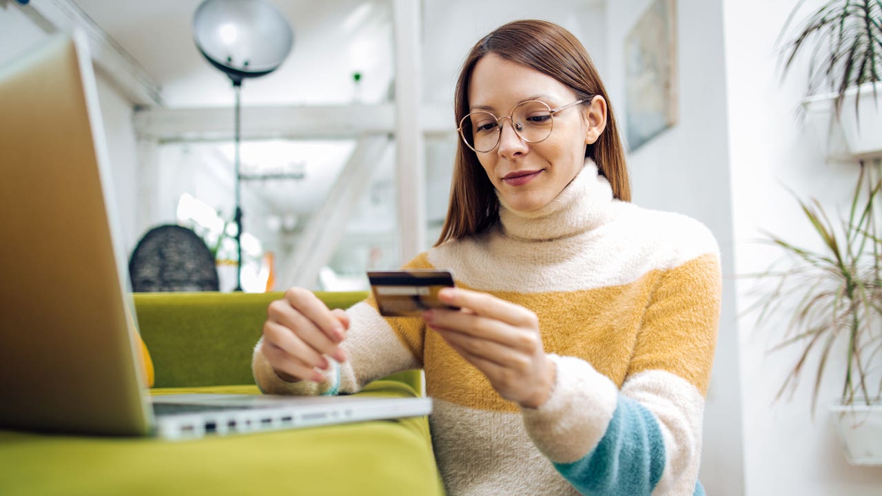 young woman looking at her credit card and working on her laptop