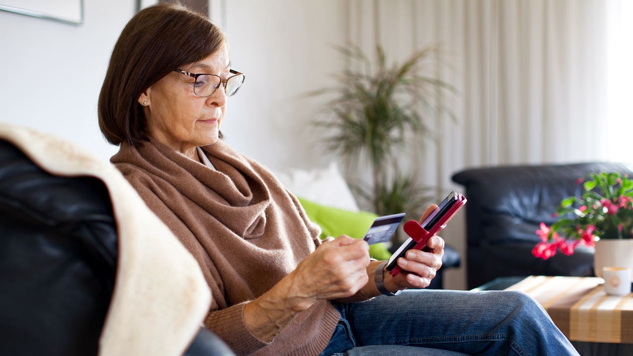 woman sitting on the couch and looking at her phone and credit card