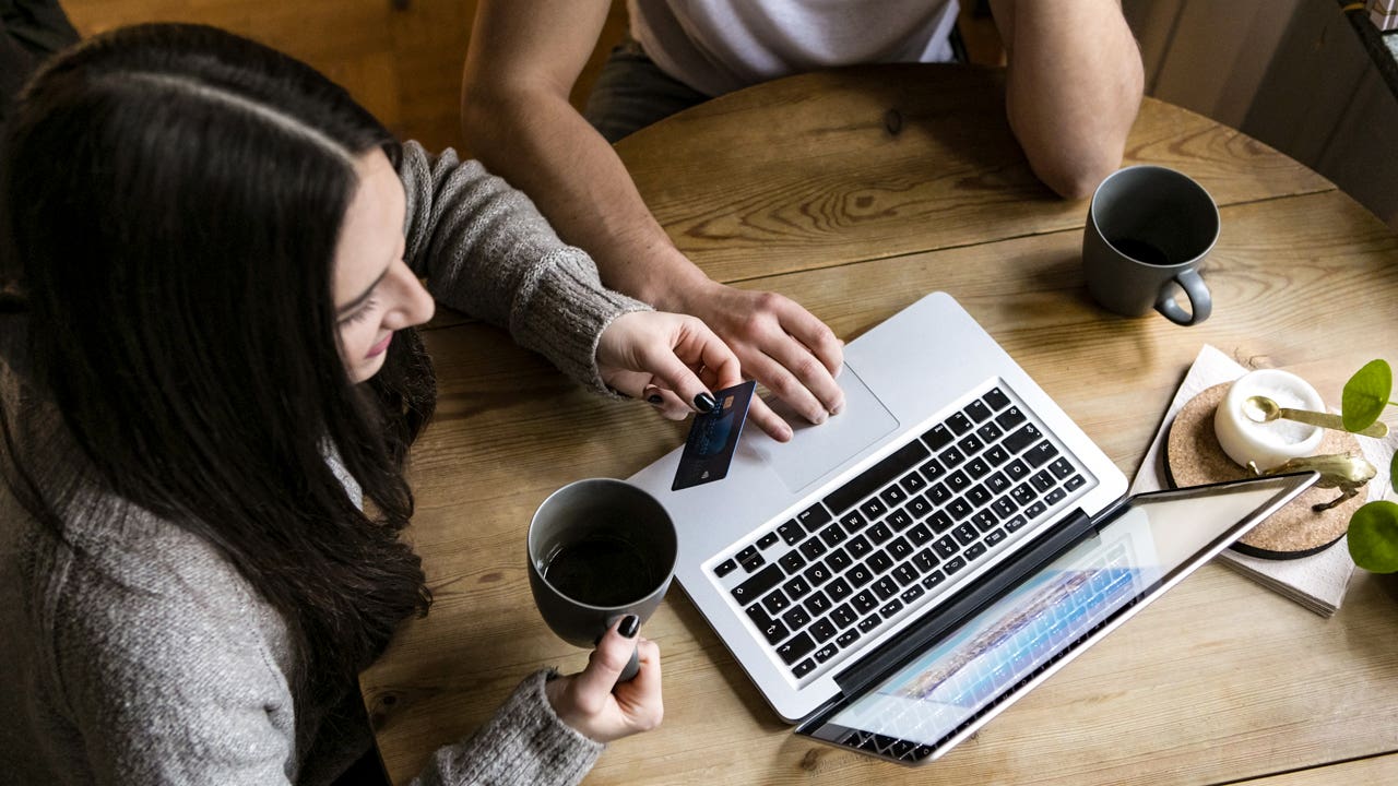 couple drinking coffee and using a credit card while on their laptop