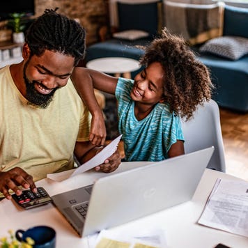 father working on finances with his daughter sitting next to him