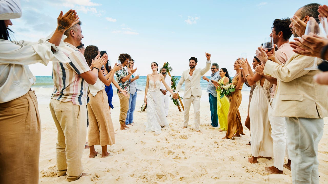 bride and groom walking down aisle after wedding ceremony on tropical beach while friends and family celebrate