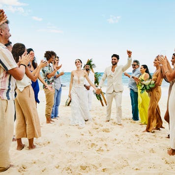 bride and groom walking down aisle after wedding ceremony on tropical beach while friends and family celebrate