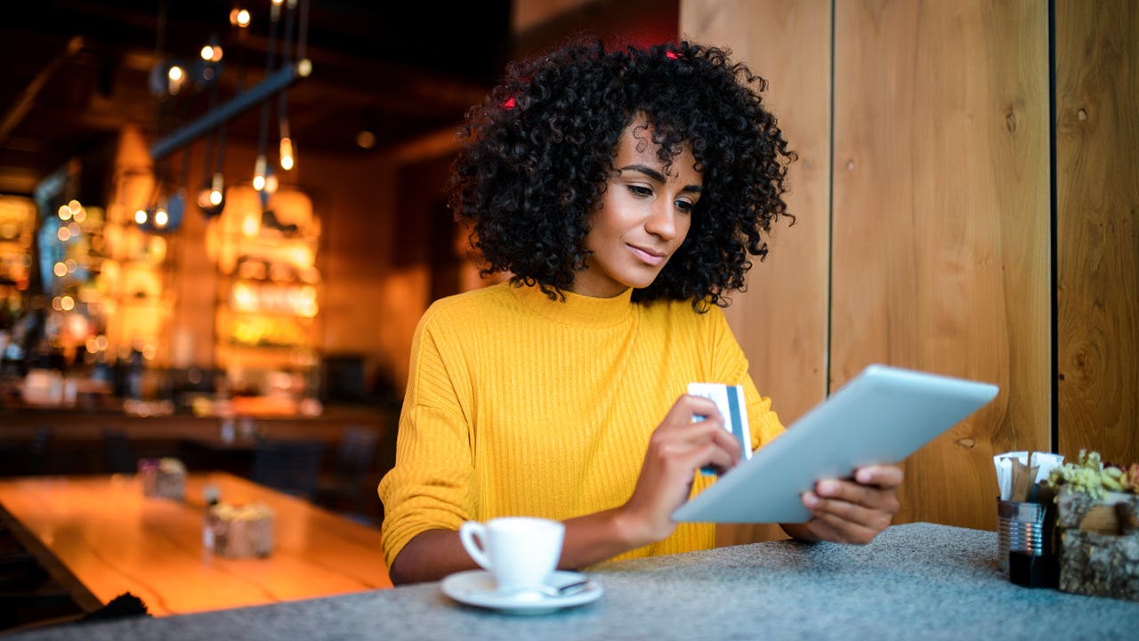 woman in a cafe using a digital tablet and holding her credit card