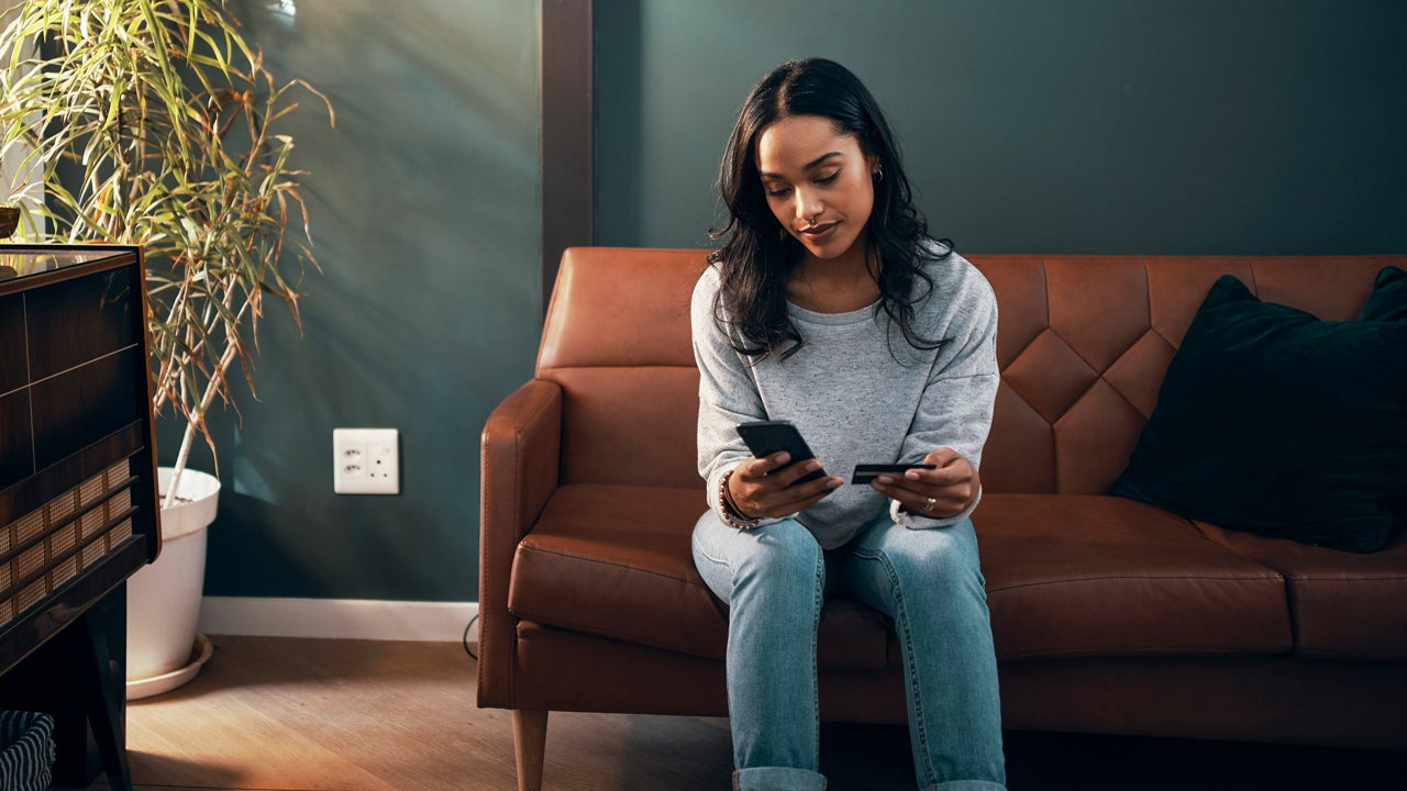 woman sitting on her couch and looking at her phone and credit card