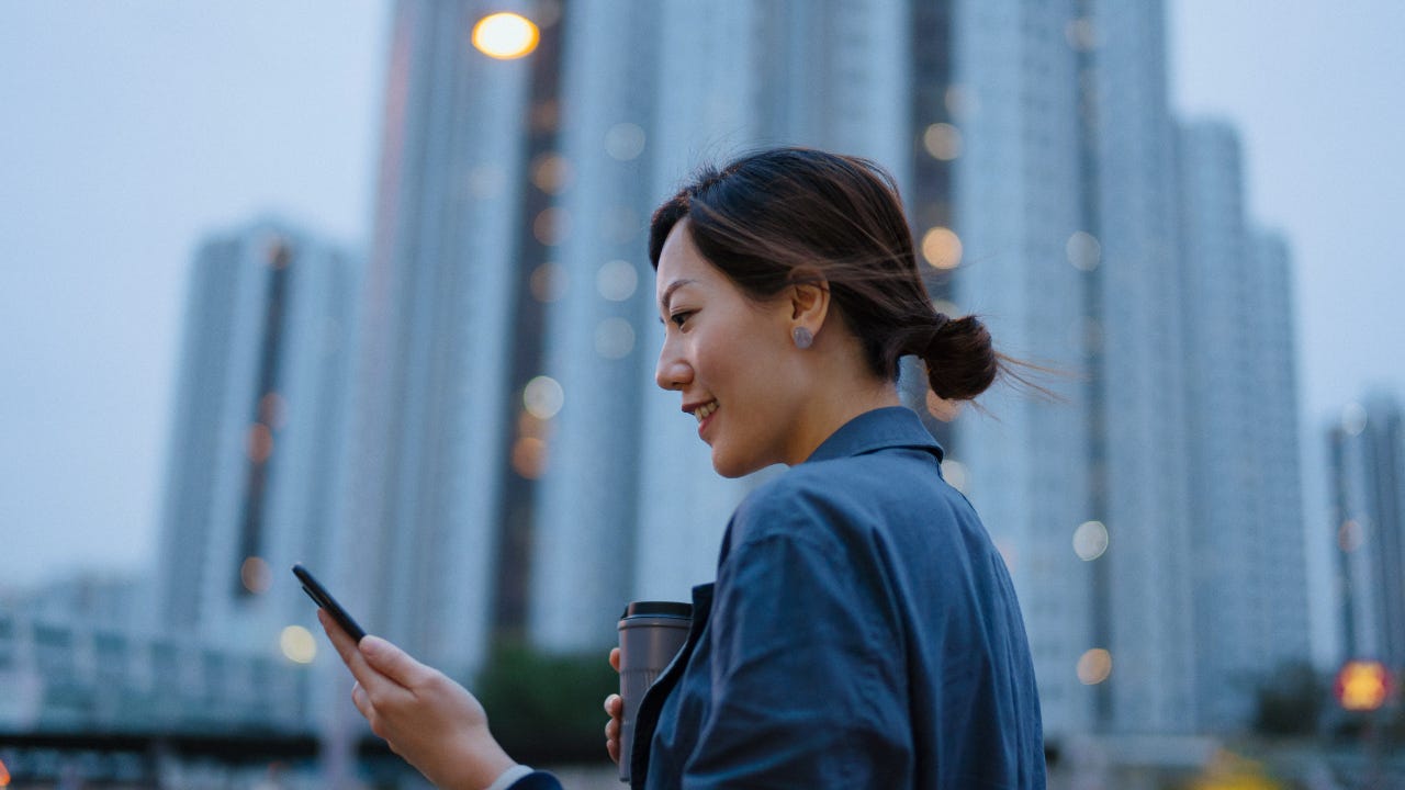 A woman walks with her phone out smiling in a downtown area