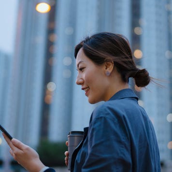 A woman walks with her phone out smiling in a downtown area