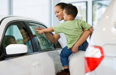 Woman holding toddler and pointing at price sticker on car