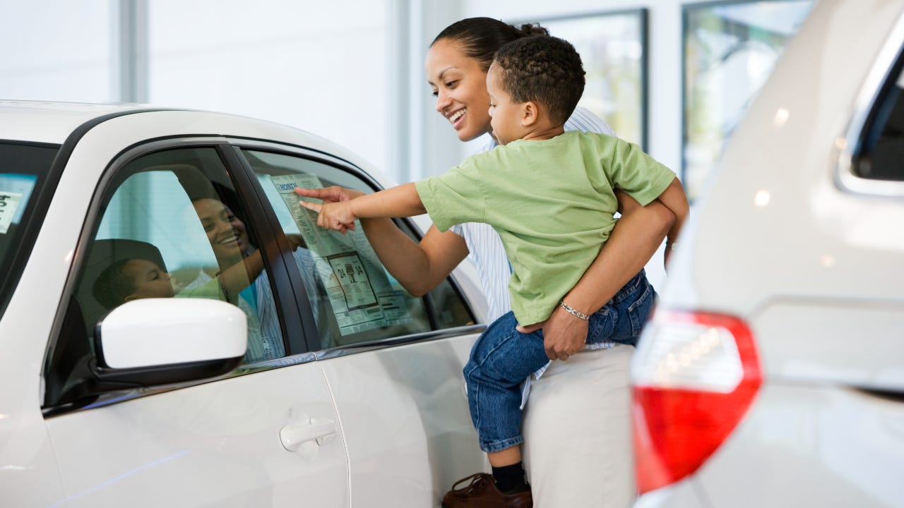 Woman holding toddler and pointing at price sticker on car