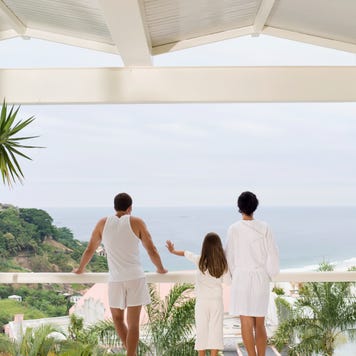 A family looks out to the sea from their house's balcony