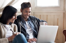 Woman and man sitting on a couch smiling at laptop