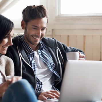 Woman and man sitting on a couch smiling at laptop
