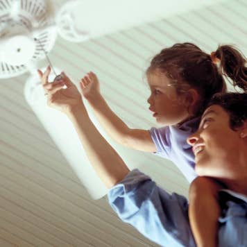 Person with a child on their shoulders, grasping ceiling fan string