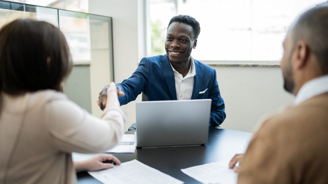 Car salesman shaking hands with customers sitting across the table from him