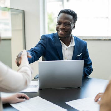 Car salesman shaking hands with customers sitting across the table from him