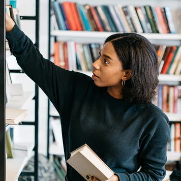 Young female african american librarian making order on bookshel