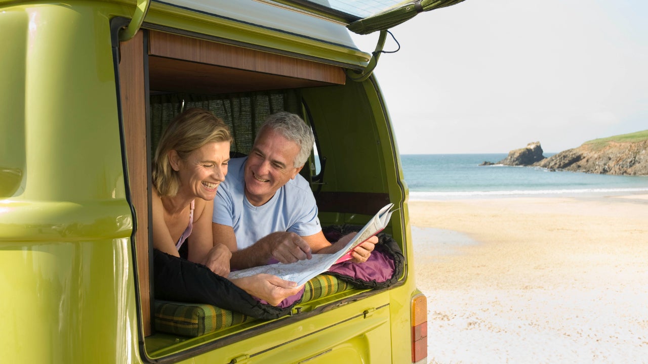 A middle-aged couple looks out to the beach from their van