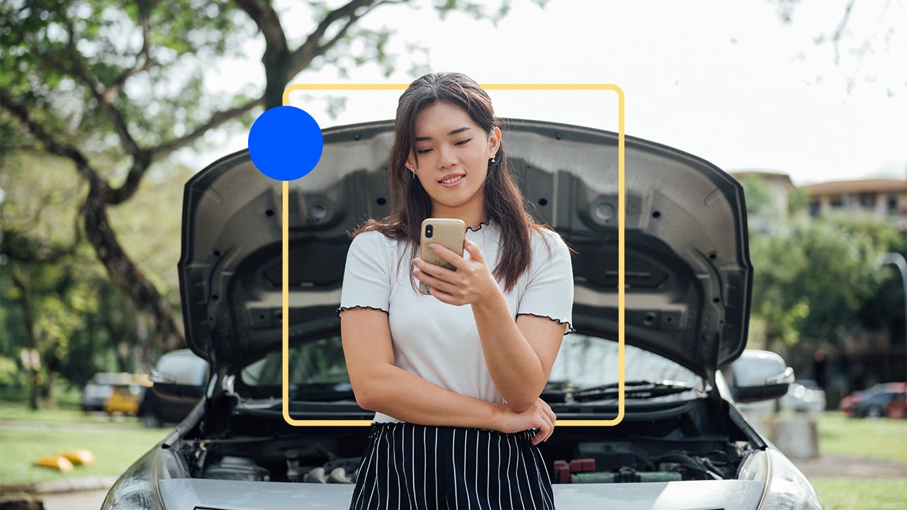 Person standing in front of car with popped trunk looking at their smartphone.