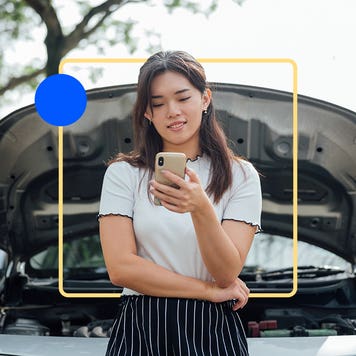 Person standing in front of car with popped trunk looking at their smartphone.