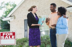 Real estate agent and a couple in front of a house for sale