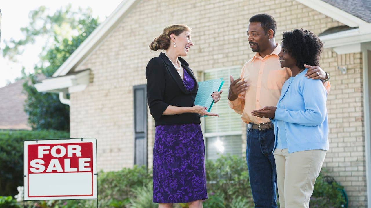 Real estate agent and a couple in front of a house for sale