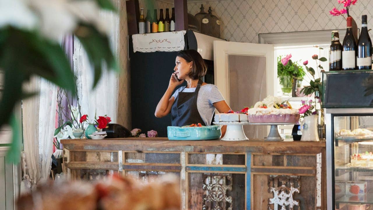 Woman talking on phone behind a counter with pastries on display