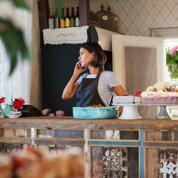 Woman talking on phone behind a counter with pastries on display