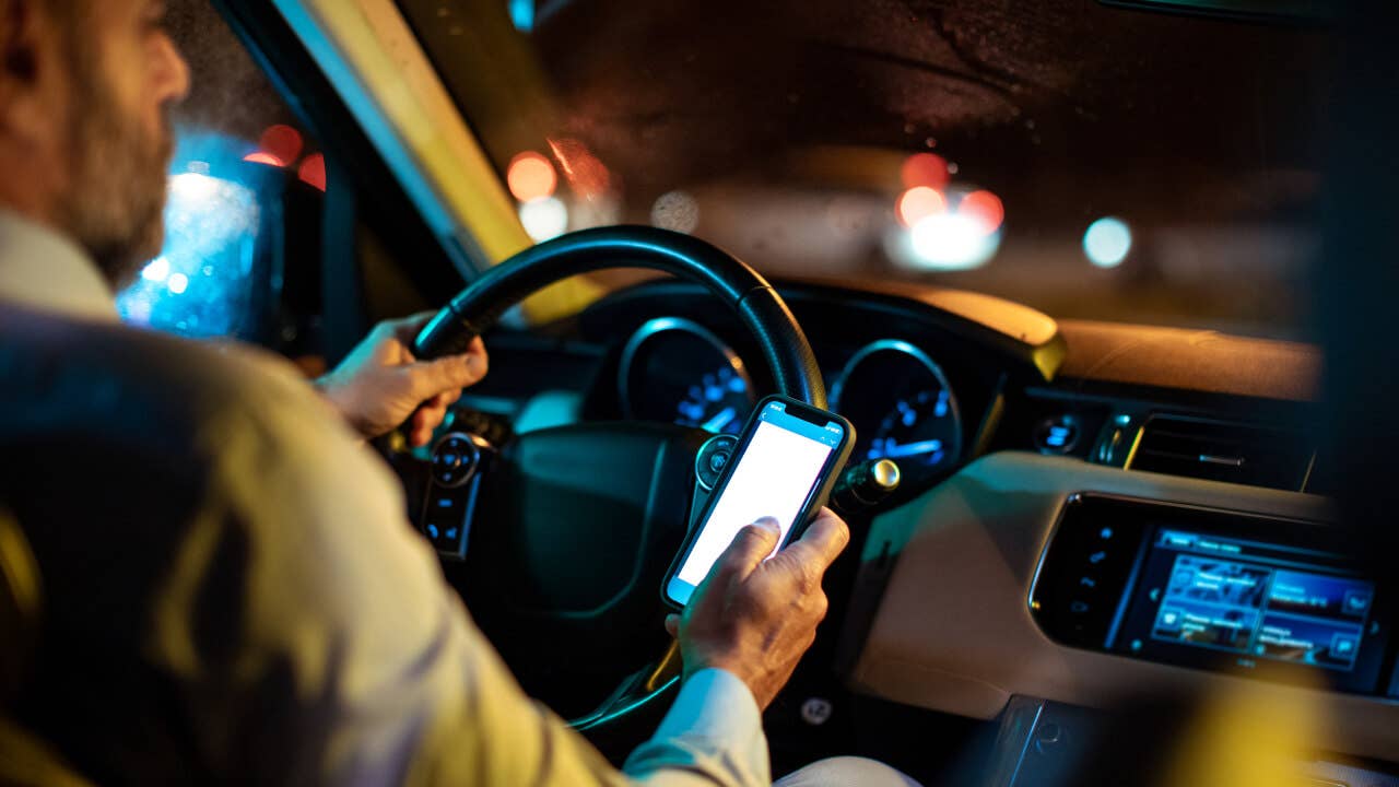 A rideshare driver looks at his phone in his car.