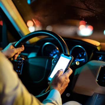 A rideshare driver looks at his phone in his car.