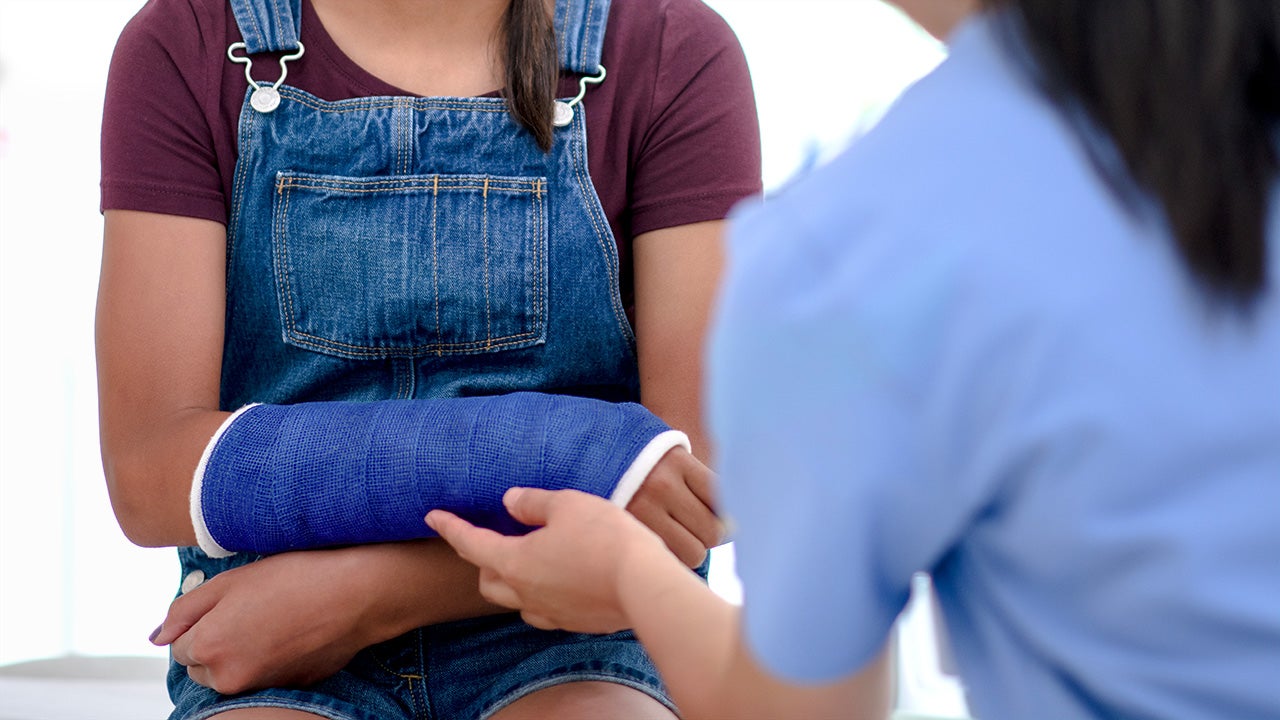 A girl of mixed race visits the nurse and has a check up on her broken arm.