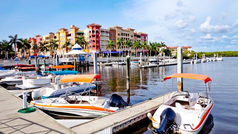 Dock and Boats overlooking Naples Bay area with condominiums and shops in background.