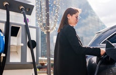 Young woman at a public electric vehicle charging station plugging in her car