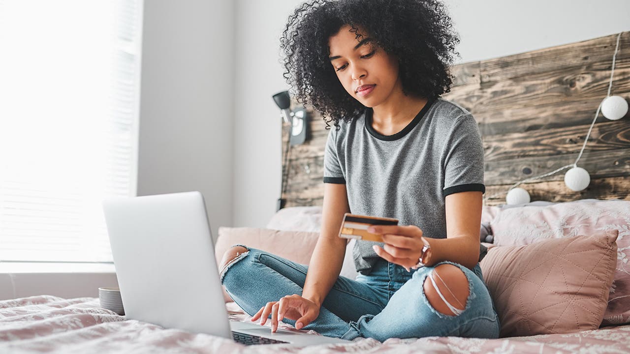 young person holding up credit card while looking at laptop