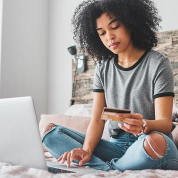 young person holding up credit card while looking at laptop