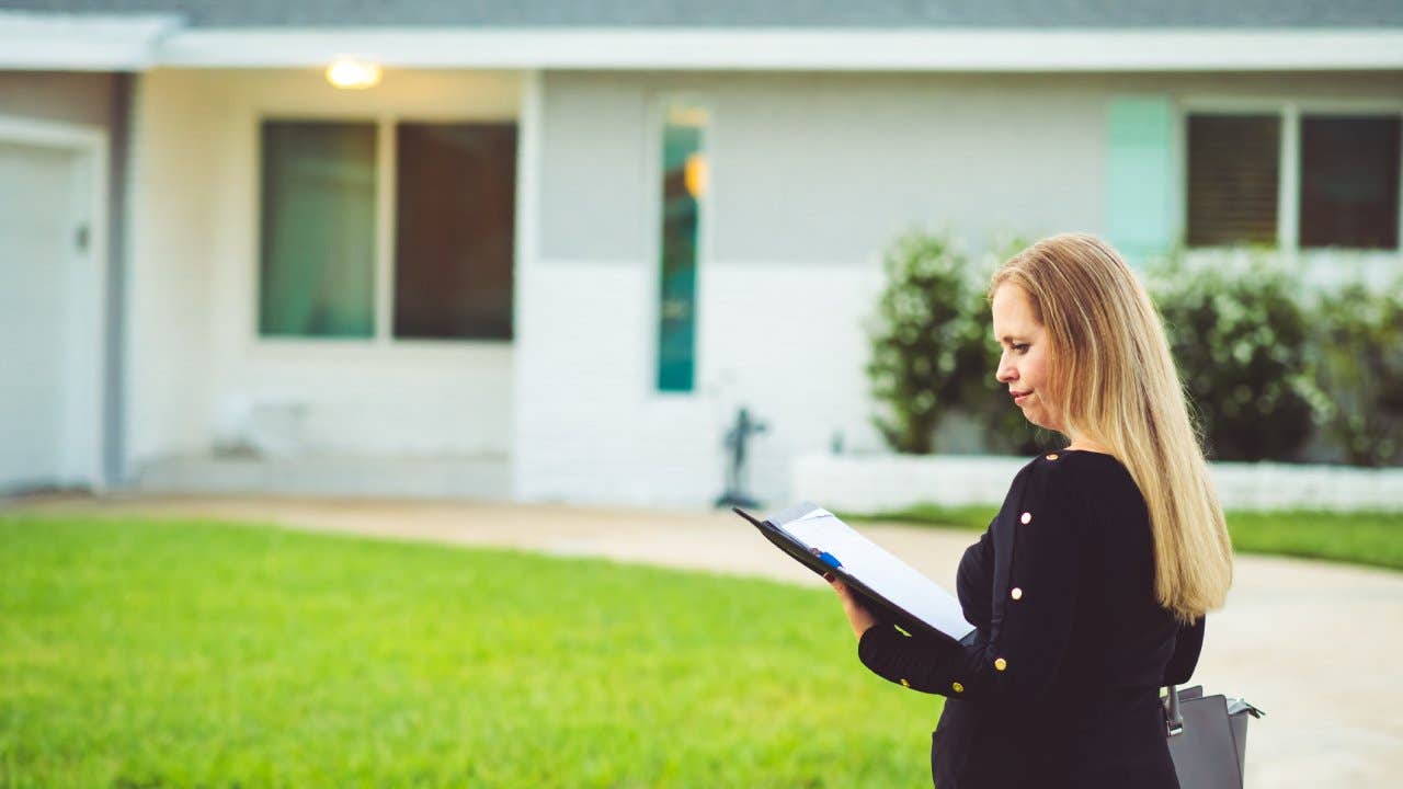 Woman walking by a house while looking at documents